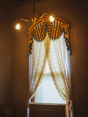 A beautifully styled window with ornate curtains and soft lighting inside a vintage room.
