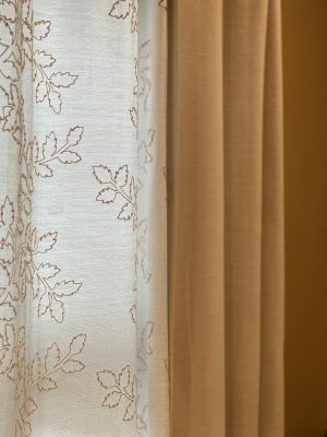 Close-up of beige and sheer curtains with leaf patterns in soft light.