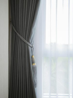 Soft gray curtain with decorative tassel tieback complemented by sheer white curtain