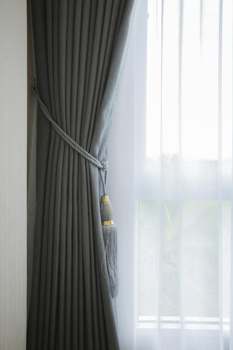 Soft gray curtain with decorative tassel tieback complemented by sheer white curtain
