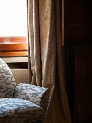 Sunlight illuminates a stylish armchair and drapes by a window, creating a warm, inviting interior scene.