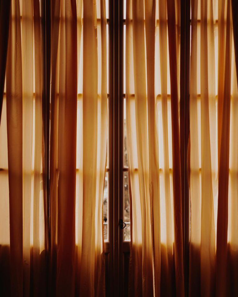 Warm sunlit curtains adorn a window in Stresa, Piedmont, creating a cozy indoor ambiance.